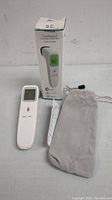 Digital forehead thermometer, box, storage pouch, and manual shown from front angle on white background.