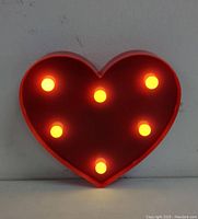 Front view of the heart-shaped lamp illuminated with six yellow-orange LED bulbs lit.