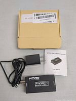 Photo showing mini 3G SDI to HDMI converter, power adapter with cable, user manual, and packaging box from top view.