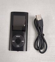 Front view of the black MP3 player with its screen turned off, showing circular control buttons, alongside bundled black USB charging cable.