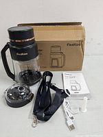 Portable blender with all components arranged: blender base with handle, blending jar, lid, USB charging cable, strap, user manual, and cleaning brush, with original cardboard box.