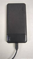 Front of black portable power bank with LED charging indicators and a connected cable.