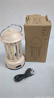 Cream beige rechargeable camping lantern with metal handle, USB cable, and original box displayed on white surface.