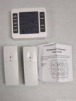Main digital thermometer unit showing temperature readings and alarm buttons, with two wireless sensor units and user manual displayed below.