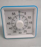 Front view of Searon visual timer showing white face with black numbers 0 to 60 and blue outer frame. Central white knob for setting time.