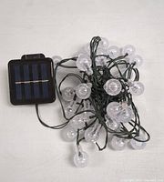 Top view of the solar light string showing clear round bulbs attached to green wire and the rectangular solar panel with black frame.