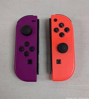 Pair of Nintendo Switch JoyCon controllers, left purple and right neon red, placed side by side on light background.