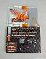 Photo of the windshield repair kit components in plastic packaging including orange injector device, resin bottles, scraper strip, rubber liner, remover blades, and instruction manual