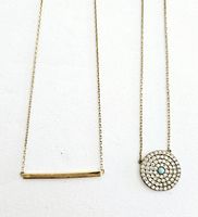 Close-up photo of two dainty necklaces, one with a horizontal bar pendant and one with a round rhinestone and turquoise stone pendant.