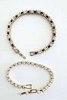 Two rhinestone bracelets laid flat, one featuring clear rhinestones and the other alternating black and clear rhinestones in gold-tone metal.