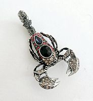 Image showing top view of the 3D scorpion brooch with a central black stone and surrounding red and champagne-colored stones.