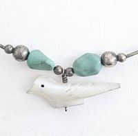 Close-up photo of mother of pearl bird pendant with turquoise beads and small round silver beads.