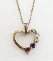 Close-up of heart-shaped sterling silver pendant with six colored gemstones arranged along one side, showing patina and wear.