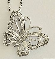 Close-up photo of the butterfly pendant showing sterling silver structure with small diamonds set around edges and open filigree design in wings.