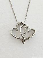 Close-up of the double heart pendant showing small diamonds on one heart and polished silver finish on the other.