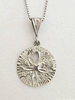 Close-up photo showing detailed silver sand dollar pendant with textured surface and cut-out design, hanging from the bail.