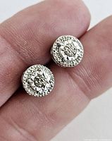 Top view close-up of round stud earrings showing central moissanite and surrounding smaller stones with detailed silver design.