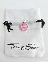 Charm resting on a white Thomas Sabo branded drawstring pouch showing the overall item and packaging.