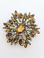 Top view of the amber color starburst brooch showing central faceted stone and surrounding rhinestones on a gold-toned metal setting.