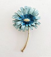 Front view of the blue flower brooch showing metal stem and blue shaded petals with yellow center.