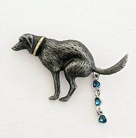 Front view of silver-tone brooch shaped like a dog squatting. Shows textured metal body and dangling blue heart-shaped gemstones from tail.