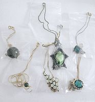 Photo showing six green themed necklaces with stones or beads on gold and silver chains inside clear plastic bags.