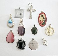 Photo showing all 11 pendants arranged on flat white surface including religious symbols, gemstone styles, and commemorative pieces.