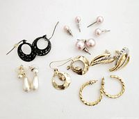Photo of eight pairs of pierced earrings laid out on a white surface showing details of each style and condition.
