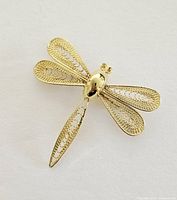 Front view of gold-tone dragonfly brooch showing detailed filigree wings and smooth body.