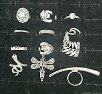 Photo showing 12 different silver tone stackable rings arranged on black felt background, various styles including floral, animal, geometric designs.