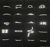 Top view photo showing all 20 silver tone stackable rings in a tray. Rings vary in design including plain bands, twisted bands, heart shapes, floral and geometric motifs.
