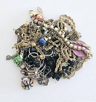 Top view of tangled assortment of jewelry showing various chains, beads and pendants including a basketball pendant and purple disc.