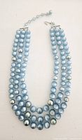 Full view of the vintage three-strand blue lucite bead necklace, showing the clasp and extender chain.