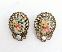Photo of vintage clip earrings showing detailed gold-tone metal filigree with oval porcelain floral design and a rhinestone.