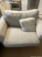 Photo of white loveseat sofa with cushions and striped pillow showing condition and overall style.