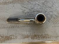 Gold-colored metal smoking pipe with soot inside bowl and black mouthpiece laid on textured surface