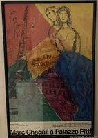 Photo of framed Marc Chagall exhibition poster with abstract figures and architectural motifs in a black frame, showing clear text at the bottom identifying the exhibition and venue.