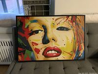 Frontal photo of a framed pop art style painting of a woman's face with abstract colorful splashes attributed to James Gill, showing vibrant colors and facial details.