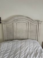Close-up of the white curved headboard of the bed frame with louvered sides and central panel