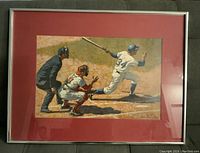 Framed, signed baseball print showing a batter swinging with catcher and umpire behind him. The print is matted in red and framed in silver.
