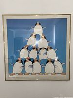 Framed art print featuring eleven penguins stacked in a pyramid arrangement on a blue background, signed by Stewart Moskowitz, dated 1977