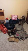 Collection of various bags on carpet including large brown bag, pink and white woven tote, black hip sack, orange bag, brown satchel, and tool belt.