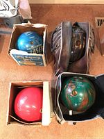Four bowling balls arranged in boxes and bags on carpeted floor.