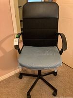 Front view of black revolving desk chair with protective plastic on seat, showing armrests and wheel base
