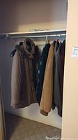 Photo showing tan and dark colored jackets and coats hanging in closet rack, including a tan winter coat and a tan suede jacket.
