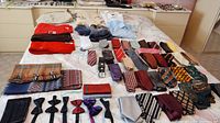 Photo showing a collection of men's bow ties, neckties, scarves, and wool sweaters arranged on a bed.