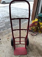 Front view of a red Milwaukee dolly truck showing curved handle, metal frame, and base plate on a concrete garage floor.