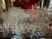 Photo of assorted clear stemmed wine and aperitif glasses arranged closely together on a table, showing a range of sizes and styles, with some decorative cuts.