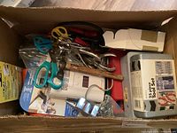 View of the box showing scissors, hammer, metal clamps, tool set, and miscellaneous items.