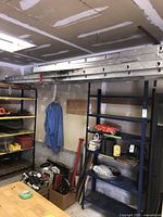 Aluminum extension ladder stored horizontally on wall brackets in a garage next to shelving units and other tools.